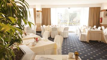Une salle à manger d’hôtel avec des tables rondes, des chaises blanches et une grande fenêtre agrémentée de rideaux.