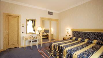 A hotel room with a large bed, a desk with a chair, a mirror, and two bedside tables with lamps.