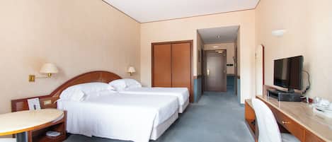 Habitación de hotel con dos camas individuales, un escritorio con silla, televisor y una mesita de noche con lámpara.