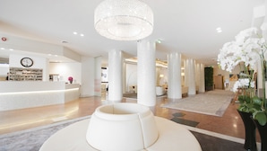 A modern hotel lobby with a reception desk, large columns, a central chandelier, and a seating area. - Hotel Excelsior San Marco (Bergamo)