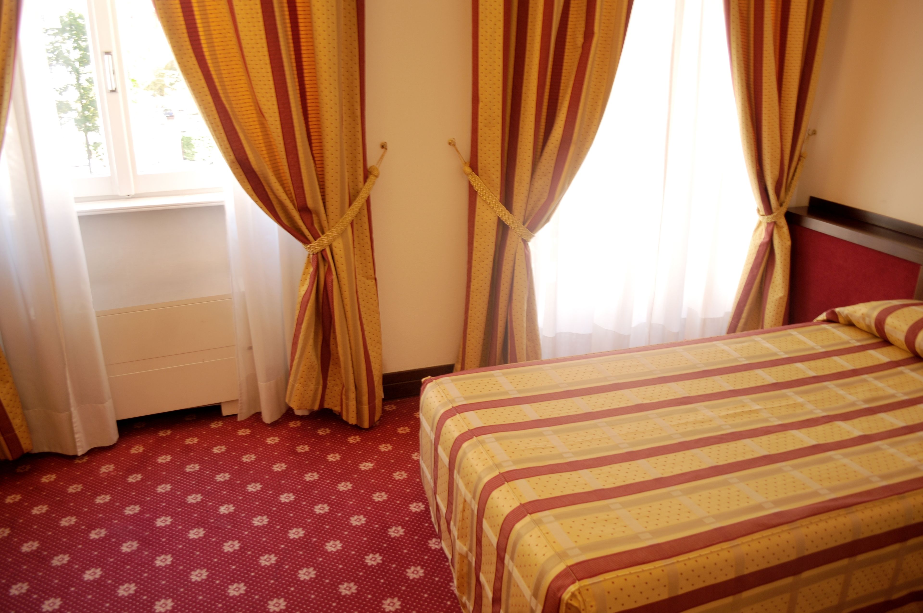 A hotel room with a bed, curtains, a radiator, and a window.