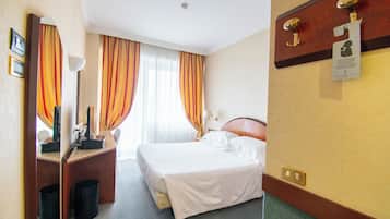 Una habitación de hotel con una cama, un escritorio con lámpara, un espejo y una lámpara de pared.