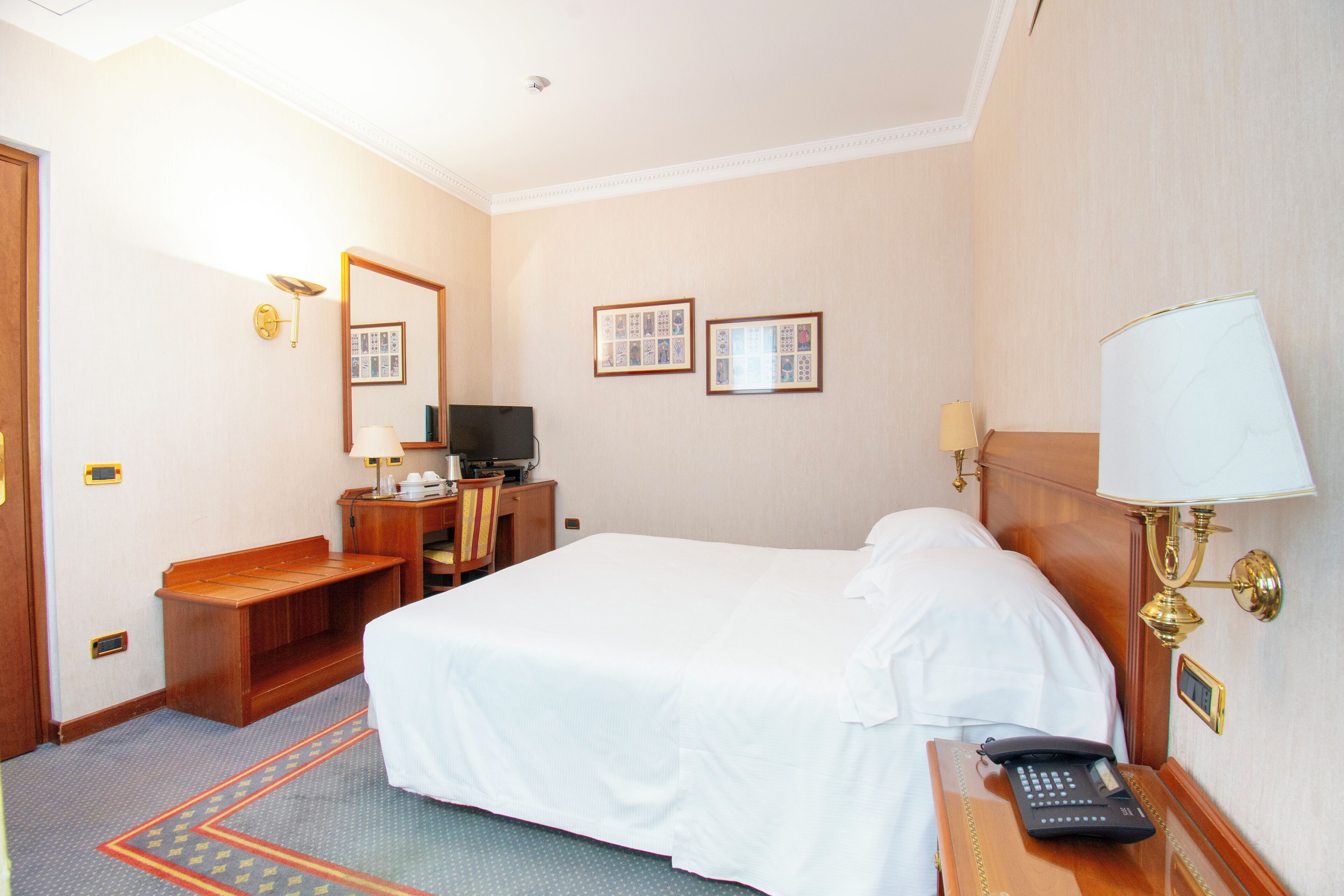 A hotel room with a bed, desk, chair, TV, and a lamp.