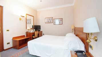 A hotel room with a bed, desk, chair, TV, and a lamp.