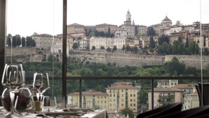 A table set with wine glasses and a candle, overlooking a historic cityscape with varied architecture and a stone wall. - Hotel Excelsior San Marco (Bergamo)