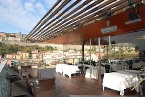 A rooftop restaurant with tables and chairs, overlooking a cityscape with historic buildings.