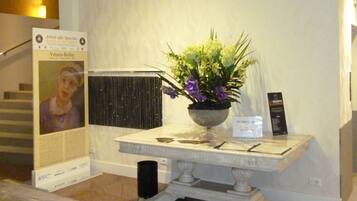 A reception area with a marble reception desk, a potted plant with purple flowers, a framed portrait, and a signboard.