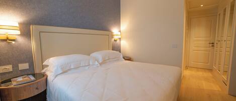 Una habitación de hotel con una cama grande, lámparas de noche, una mesita de madera y una puerta que da a otra habitación.