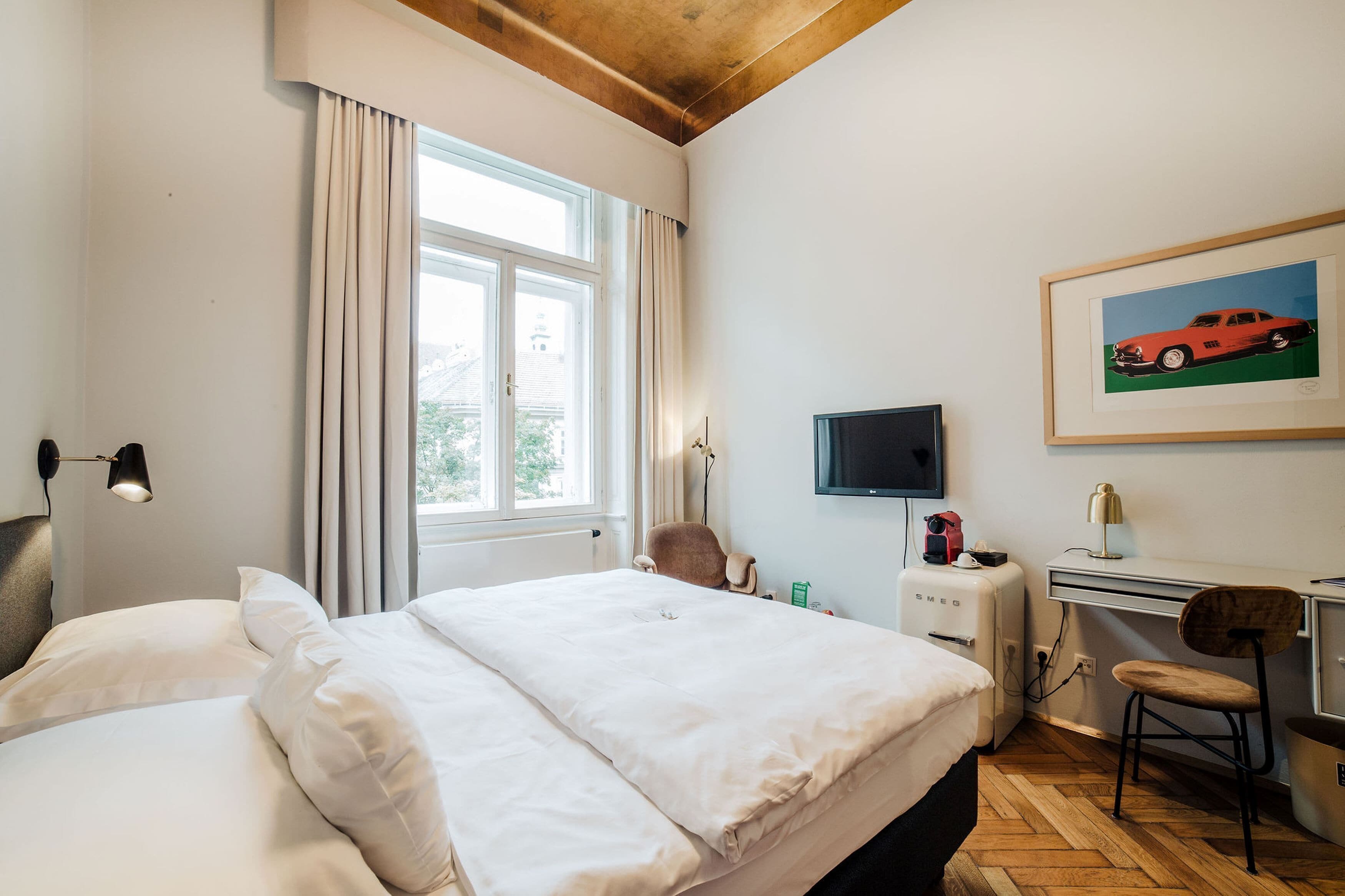 Ett hotellrum med en säng, ett skrivbord, en stol, en tv och ett fönster med gardiner.