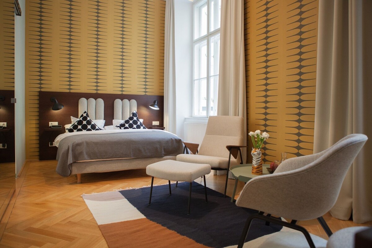 A modern bedroom with a bed, two chairs, a small table, and a vase of flowers.