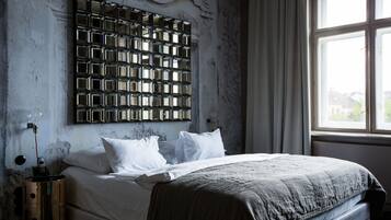 Een slaapkamer met een groot bed, een hoofdeinde met een geometrisch patroon, een nachtkastje met een lamp en een raam met gordijnen.