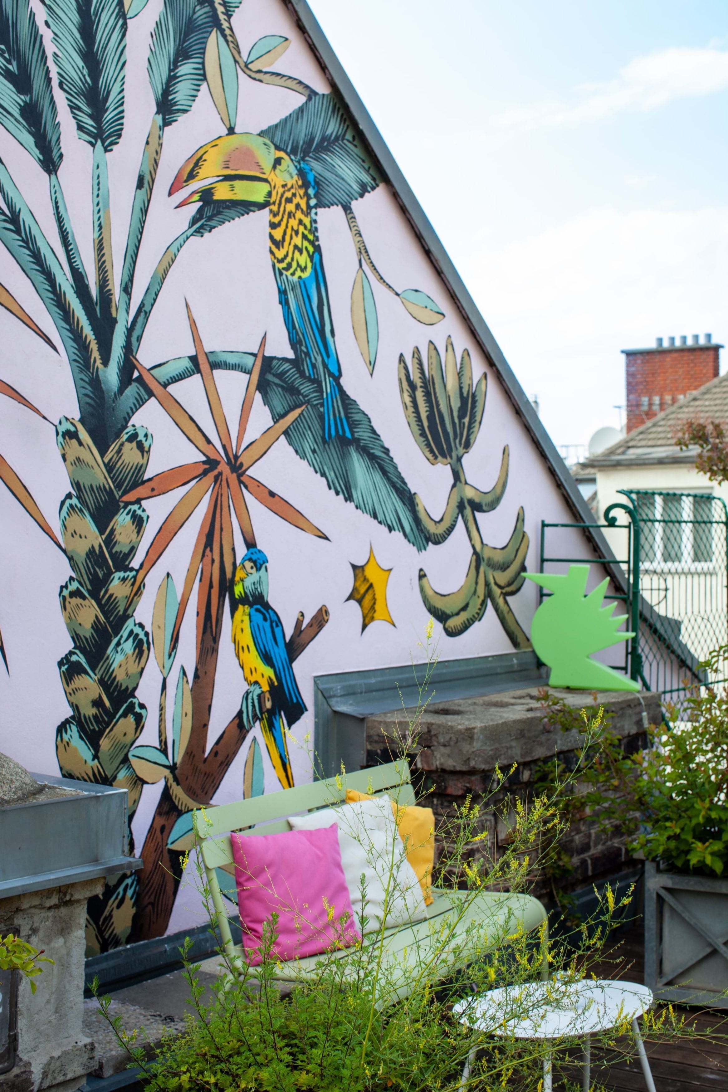 Een muurschildering met een ontwerp van een vogel en planten op een gevel.