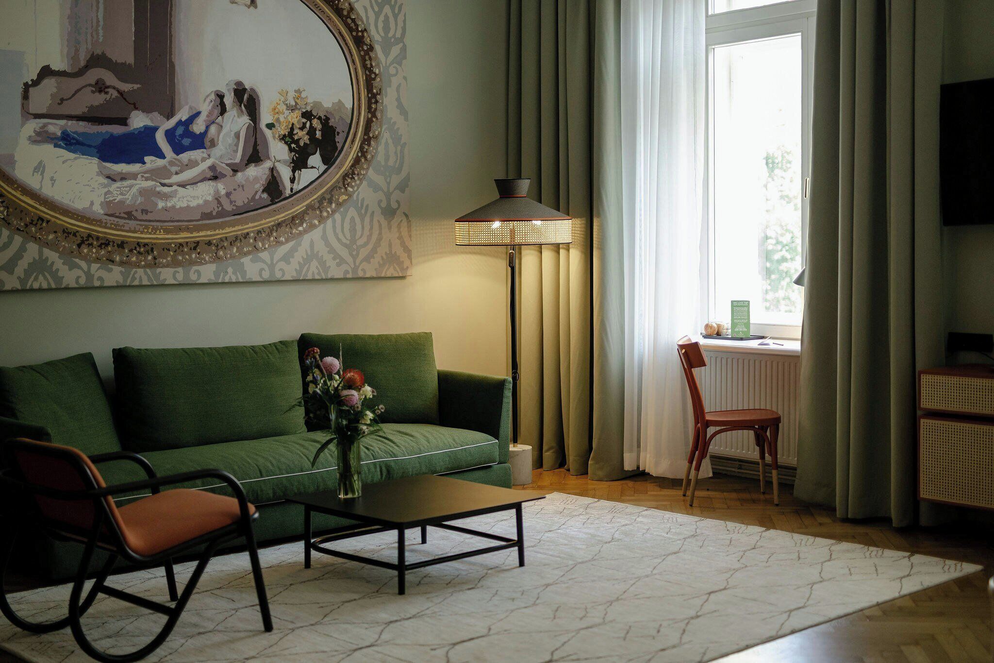 A living room with a green sofa, a coffee table, a chair, a floor lamp, and a painting on the wall.