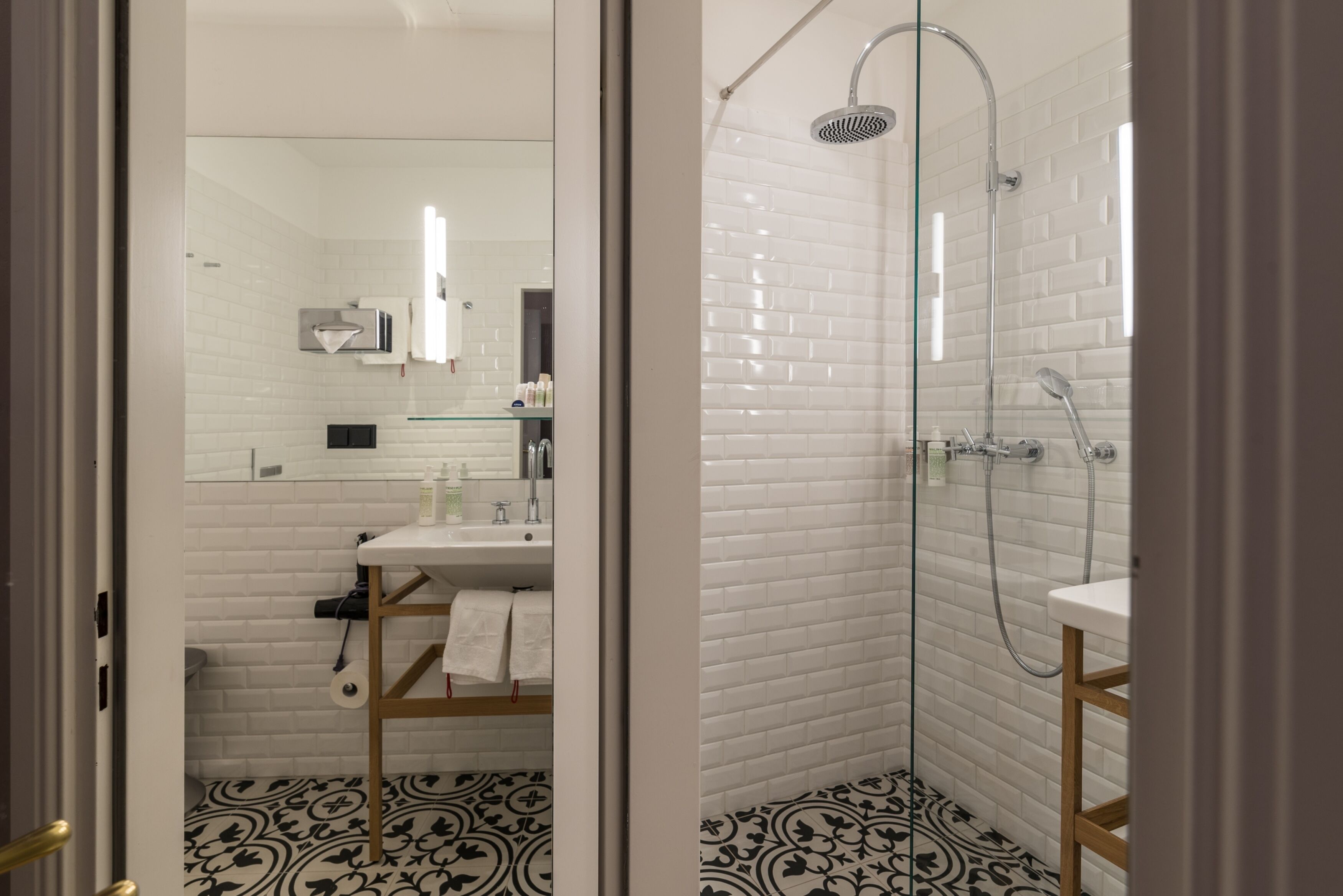 Un baño moderno con azulejos blancos tipo metro, ducha con mampara de vidrio y baldosas estampadas.