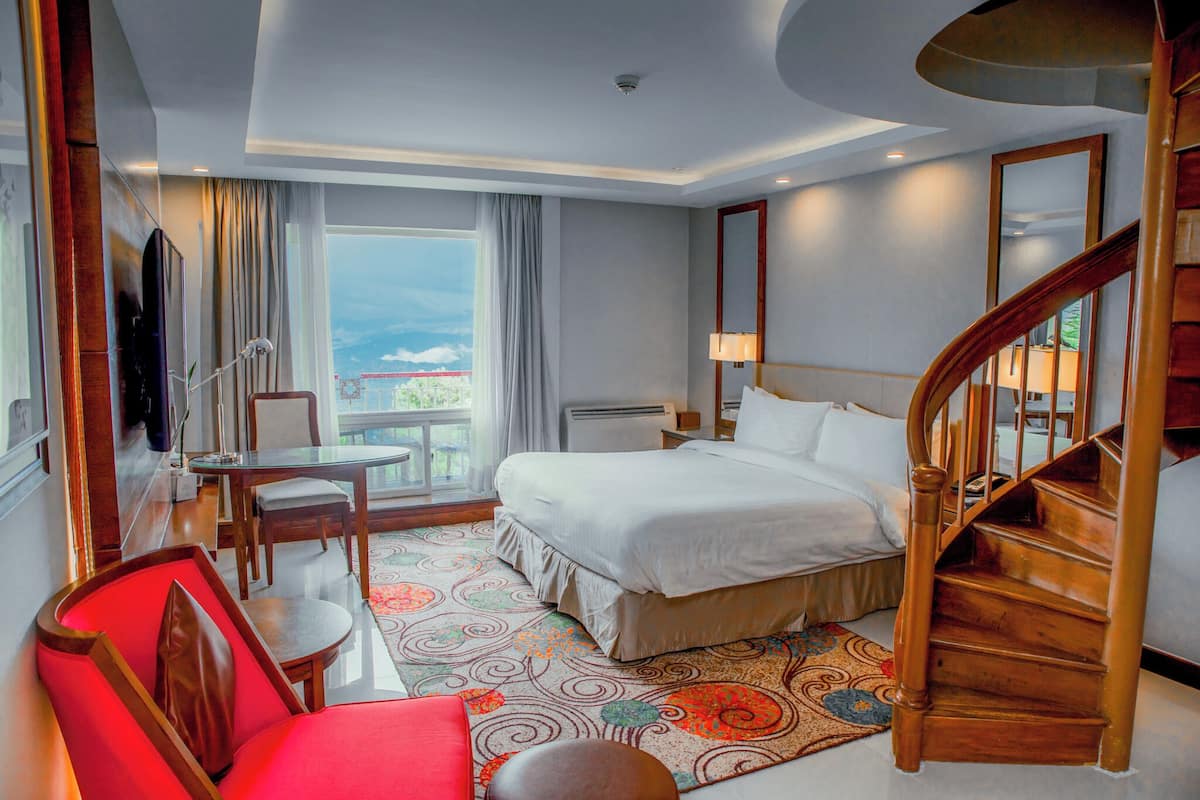 Une chambre d’hôtel comprenant un lit, un bureau, une chaise, une télévision, un escalier et une vue sur l’extérieur.
