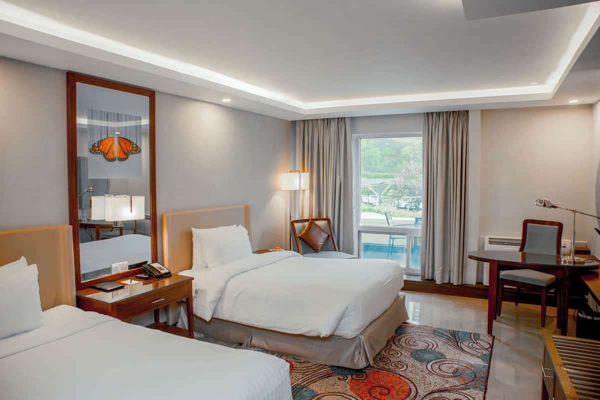 Une chambre d’hôtel avec deux lits, un bureau avec un téléphone, une chaise, une lampe de bureau et une vue sur l’extérieur.