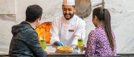 A restaurant with a marble countertop, hanging pendant lights, and a chef preparing food.