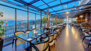 A restaurant with a long table and chairs, large windows, and a view of the city.