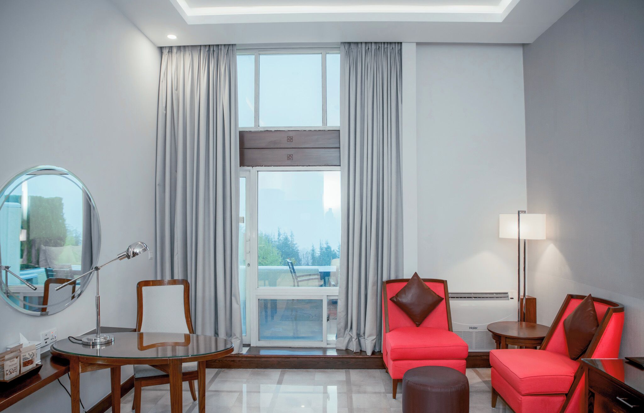 Habitación de hotel con una mesa de vidrio, una silla, un sofá, una lámpara y vistas al exterior.