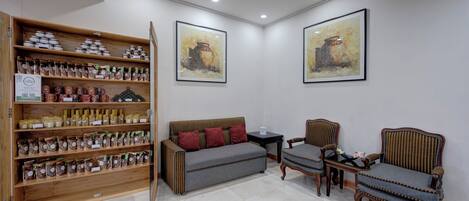 A room with a sofa, two chairs, a coffee table, and a bookshelf filled with jars.