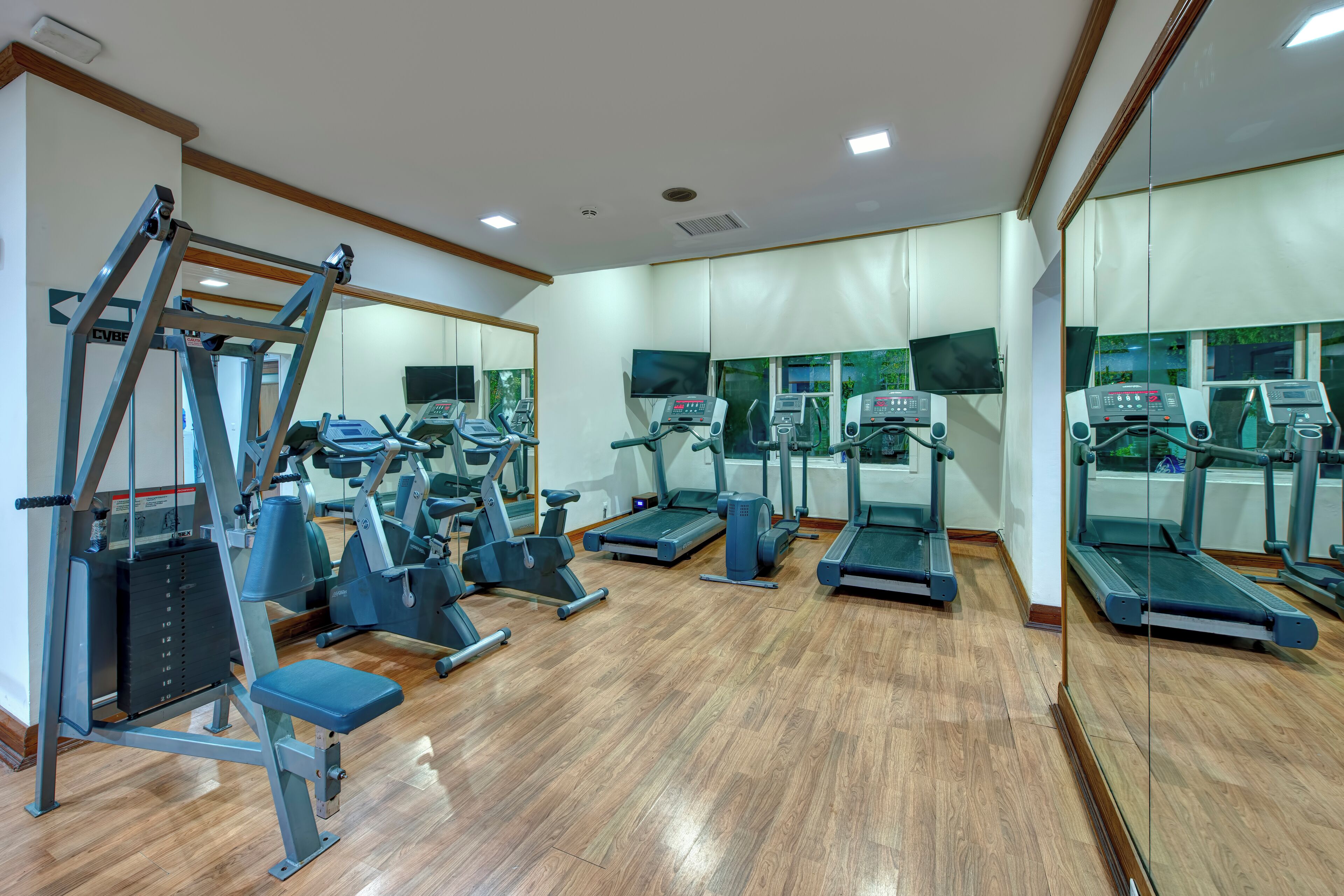 A gym with exercise equipment, wooden flooring, and mirrors on the walls.