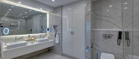 A modern bathroom with two sinks, a large mirror, a glass shower enclosure, and a toilet.