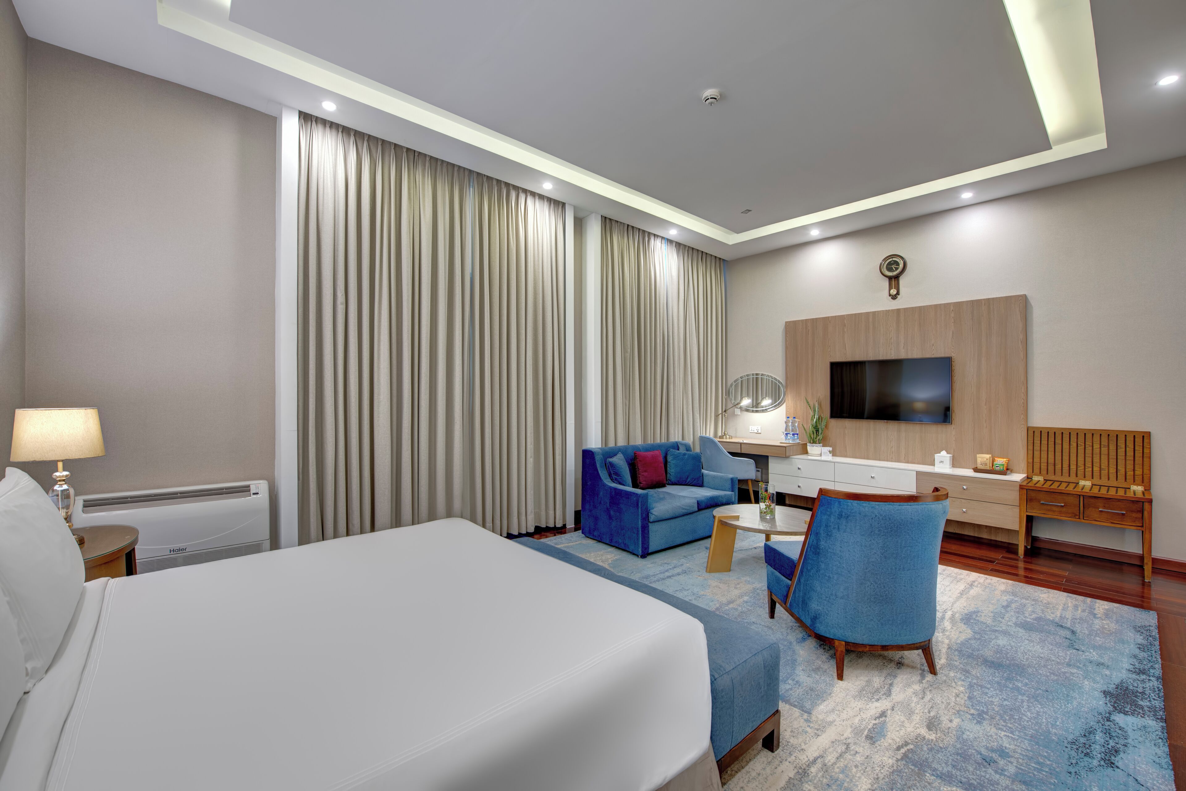 A hotel room with a bed, a blue sofa, a desk, a chair, a TV, and a window with curtains.