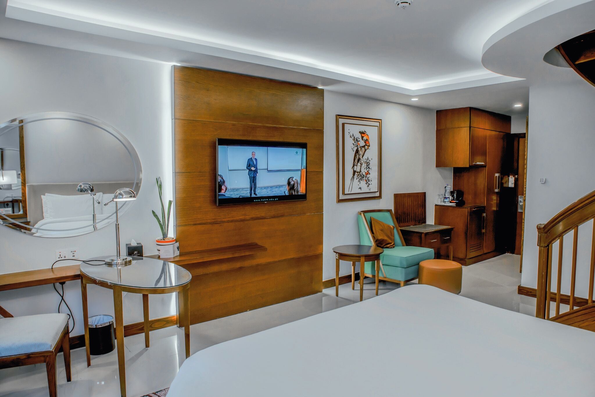 Una habitación de hotel moderna con una cama grande, un televisor montado en la pared, un armario de madera, una mesita y una silla.