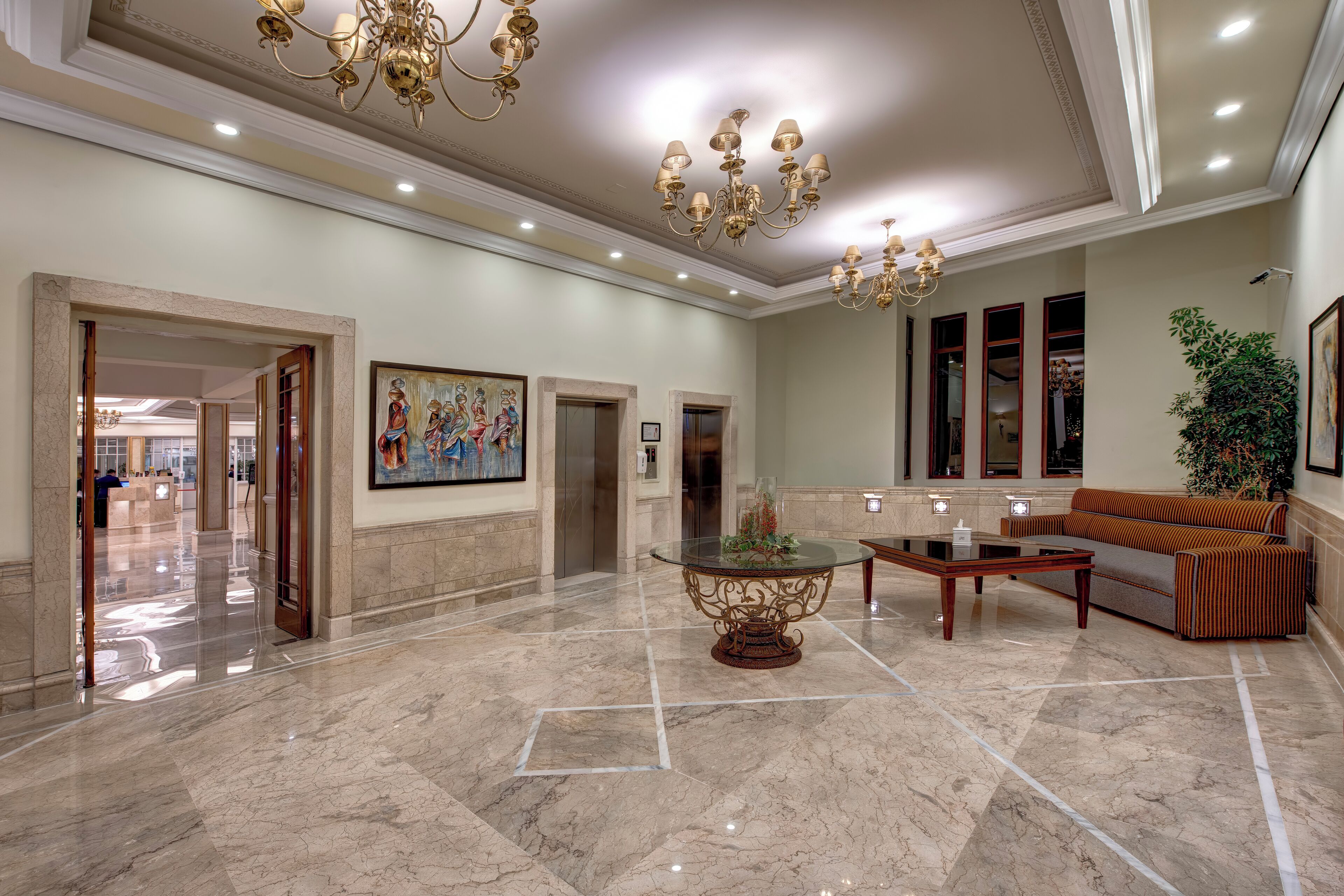 A spacious lobby with a marble floor, a central ornate table, a sofa, and a chandelier.