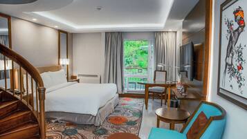 Ein Hotelzimmer mit Bett, Schreibtisch, Stuhl, Fernseher, einer Treppe und einem Balkon mit Blick auf Grünflächen.