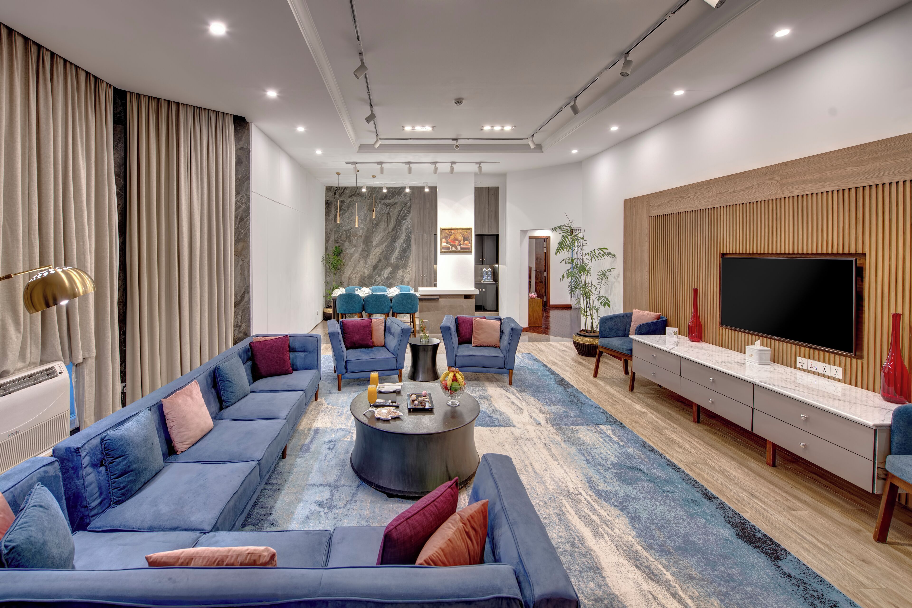 A modern living room with a sofa set, a coffee table, a TV, and a kitchen area in the background.