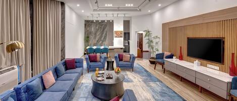 A modern living room with a sofa set, a coffee table, a TV, and a kitchen area in the background.