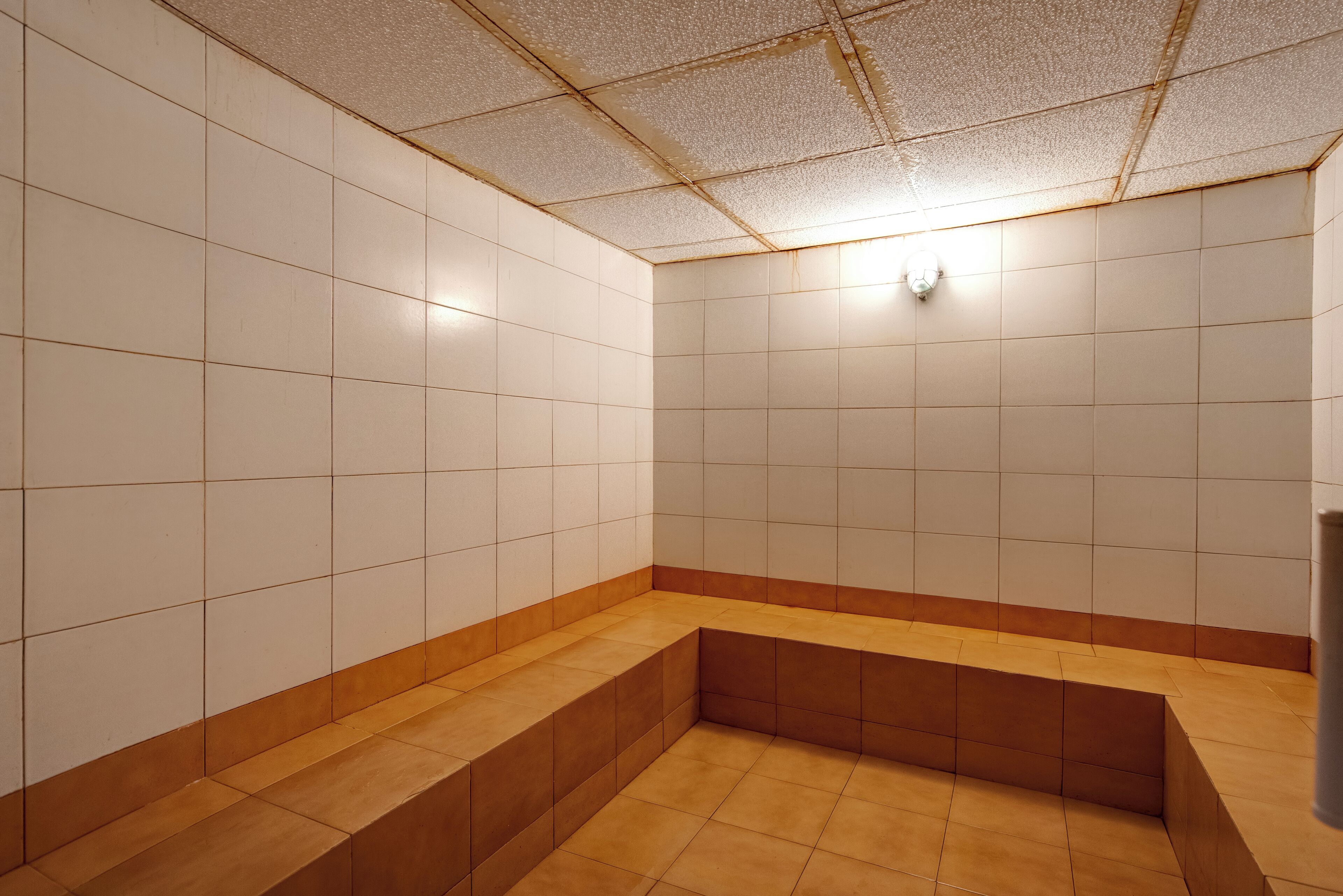 Un baño con piso de azulejos, un banco y una lámpara en el techo.