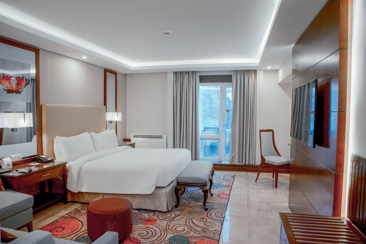Une chambre d’hôtel avec un grand lit, un bureau avec un téléphone, une chaise, une télévision et une vue sur l’extérieur.
