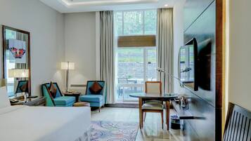 Habitación de hotel con cama, dos sillones, una mesita, televisor y ventana con cortinas.
