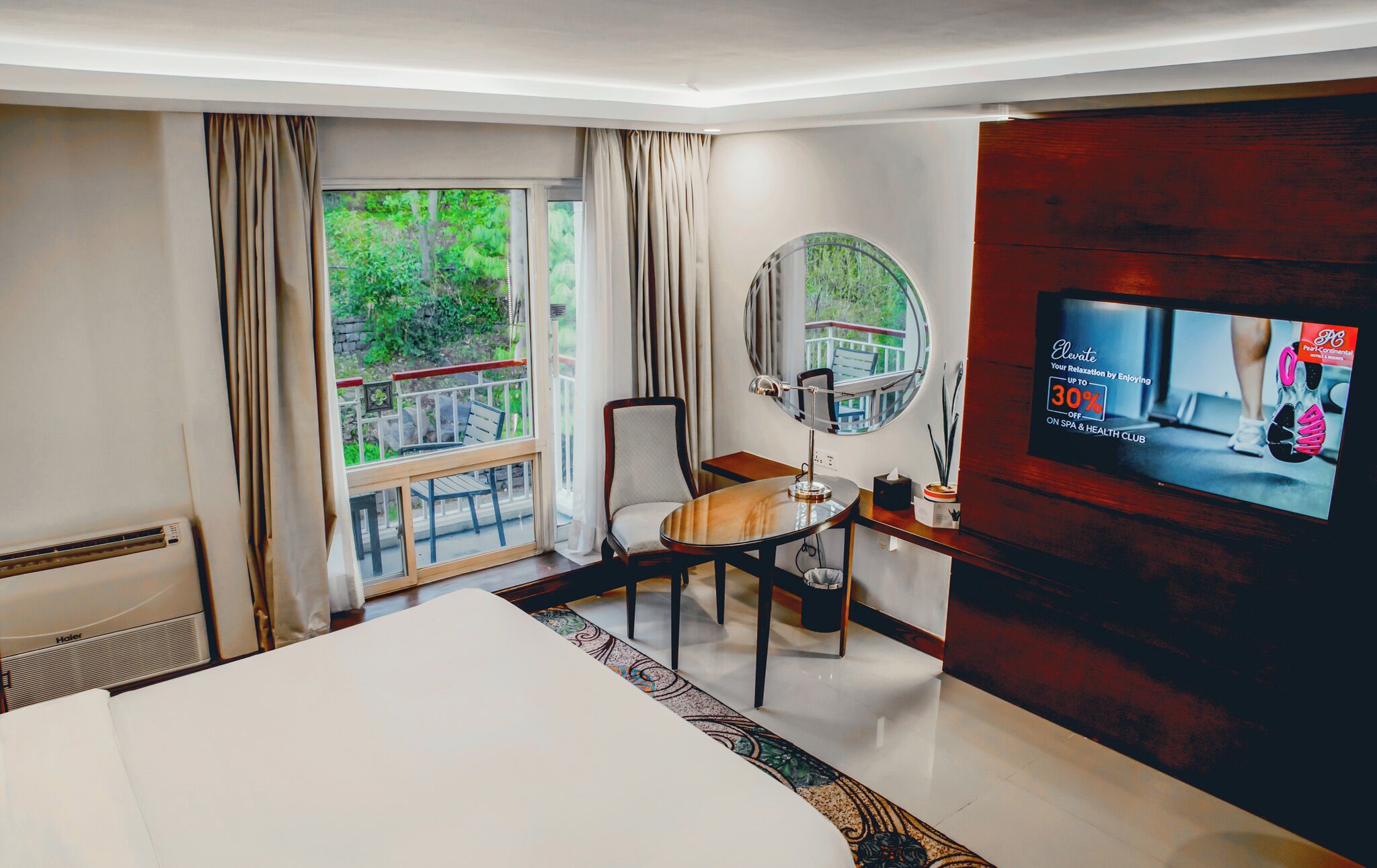 Habitación de hotel con cama, escritorio, silla, televisor y ventana con cortinas.