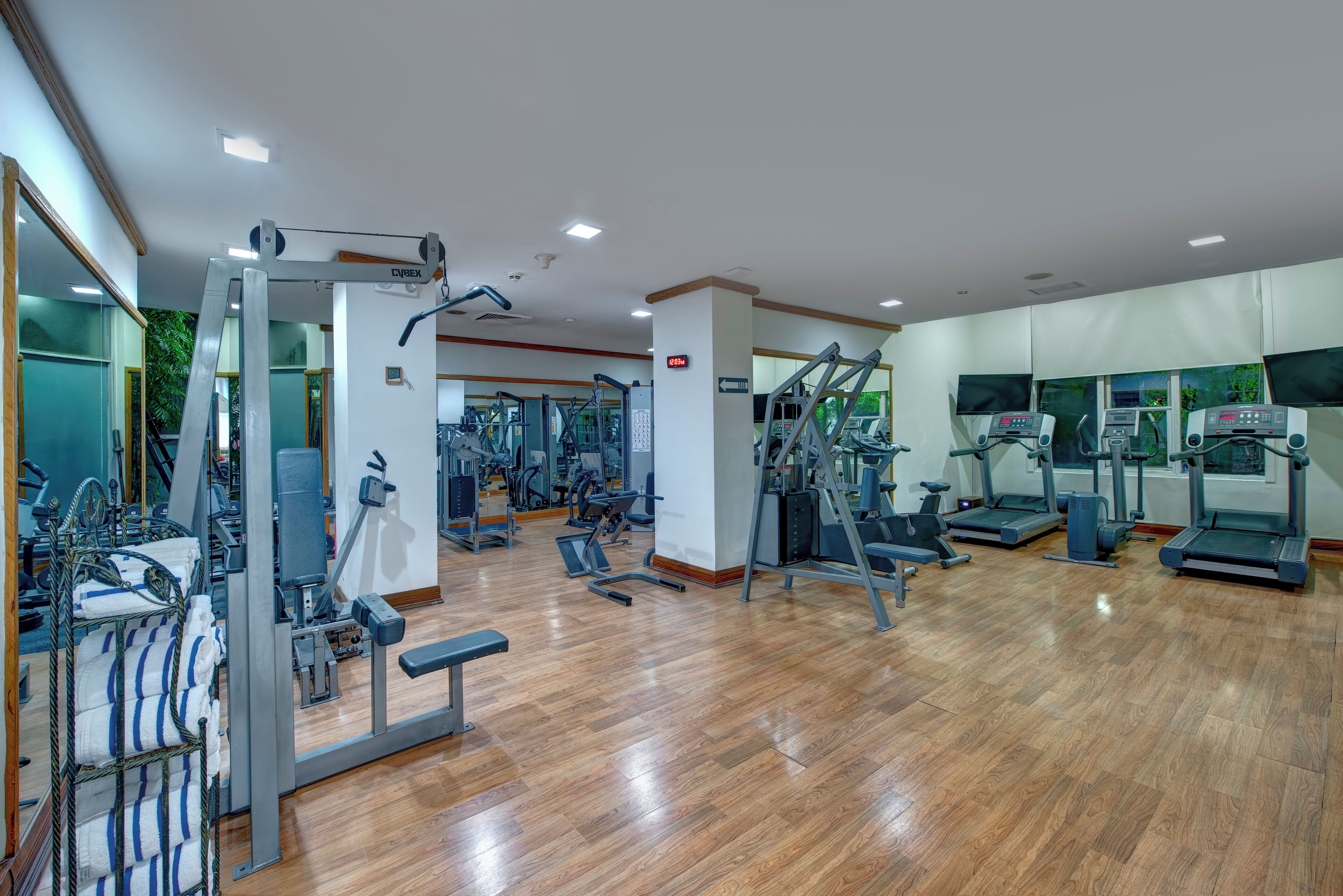 A spacious gym with various exercise equipment, including treadmills and weight machines, and a wooden floor.