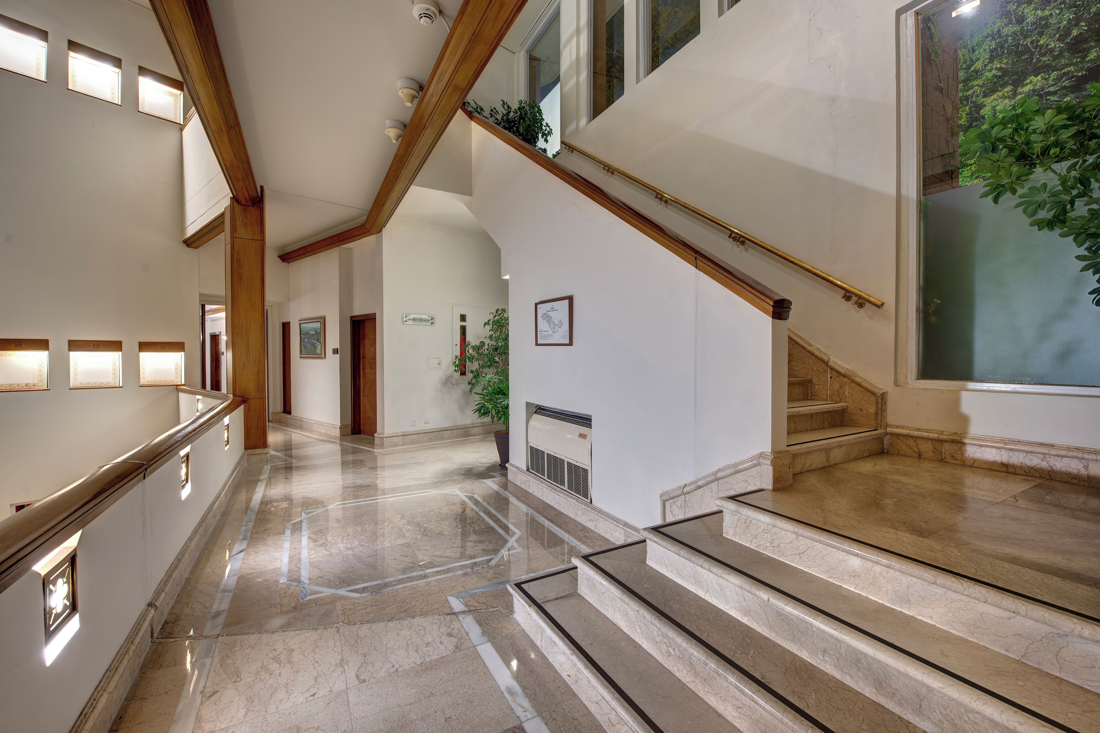 A spacious hallway with a marble floor, wooden beams, and a staircase with a glass railing.