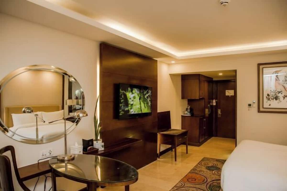 A hotel room with a bed, a desk with a chair, a TV, a mirror, and a small table.