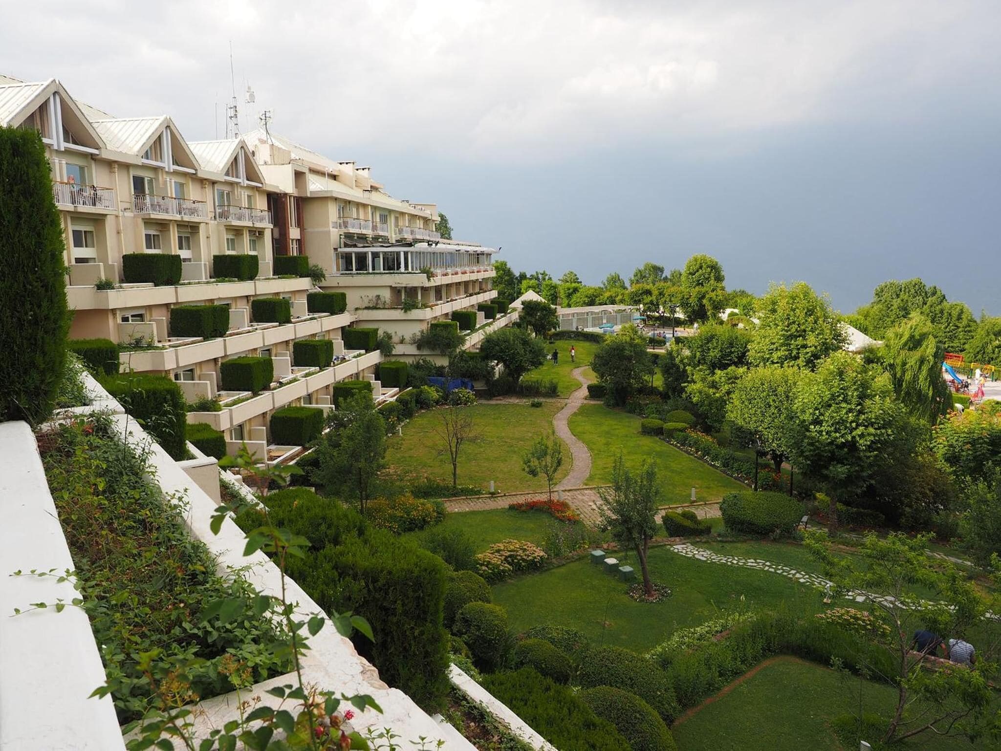 A multi-story hotel with balconies, a well-maintained garden, and a clear sky.