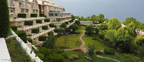 A multi-story hotel with balconies, a well-maintained garden, and a clear sky.