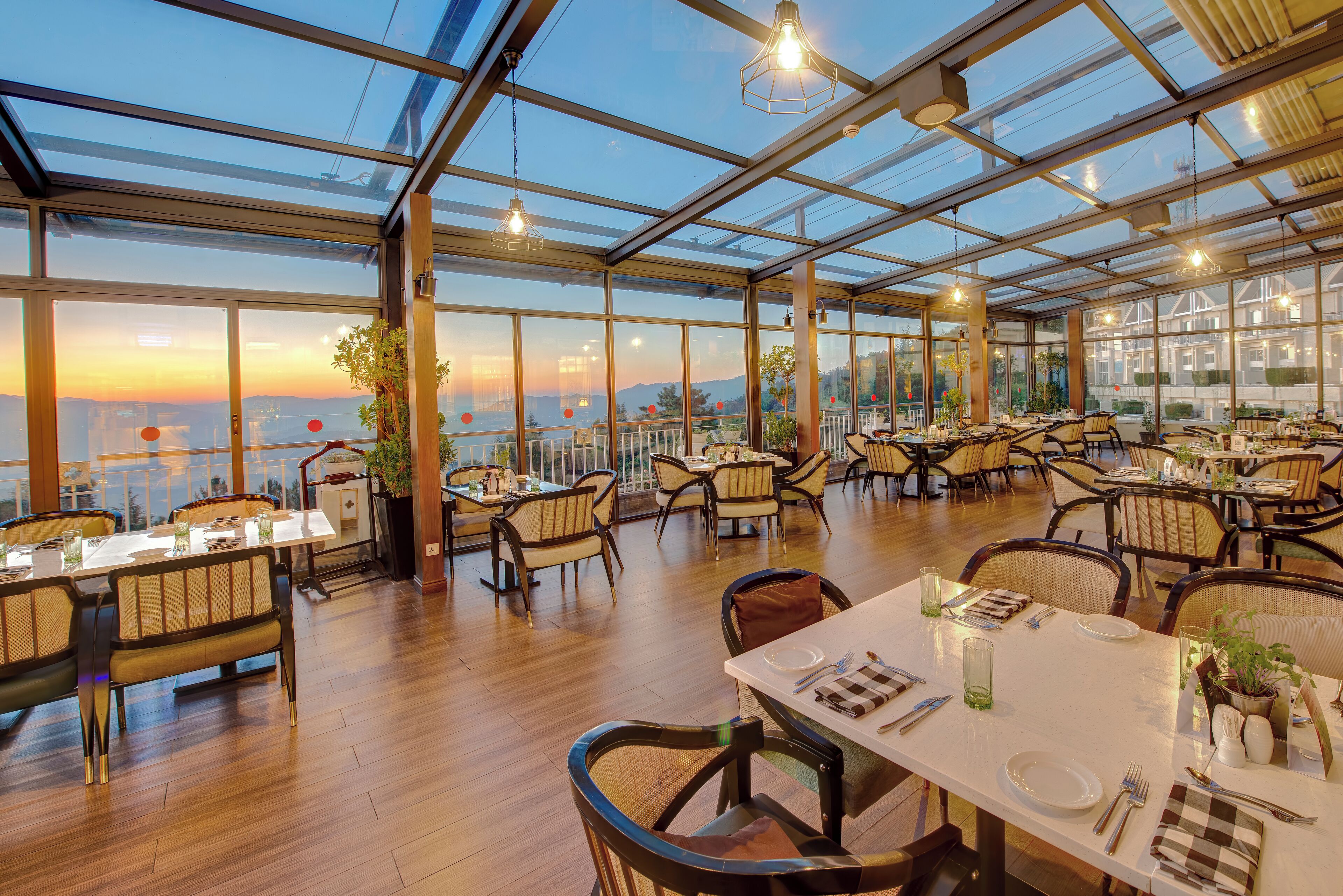 A spacious restaurant with high ceilings and large windows, offering views of the sunset and cityscape.