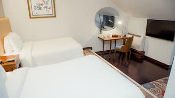 Ein Hotelzimmer mit zwei Betten, einem Schreibtisch mit Stuhl, einem Fernseher und einem runden Spiegel.