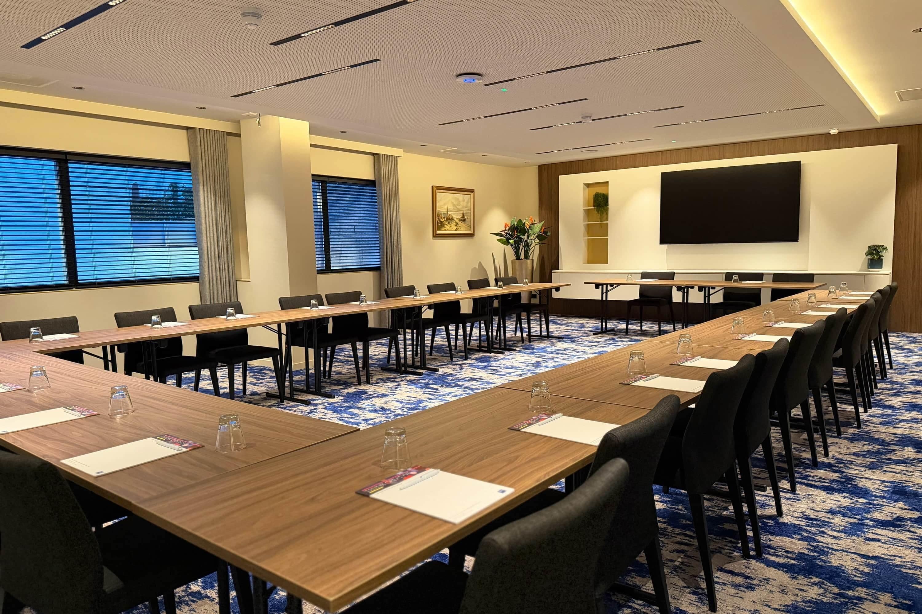A conference room with a long table, chairs, a projector screen, and a large window with blinds.