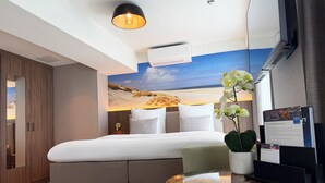 A hotel room with a bed, a desk with a computer, a potted orchid, and a wall mural. - TRYP by Wyndham Badhotel The Hague Scheveningen (The Hague)