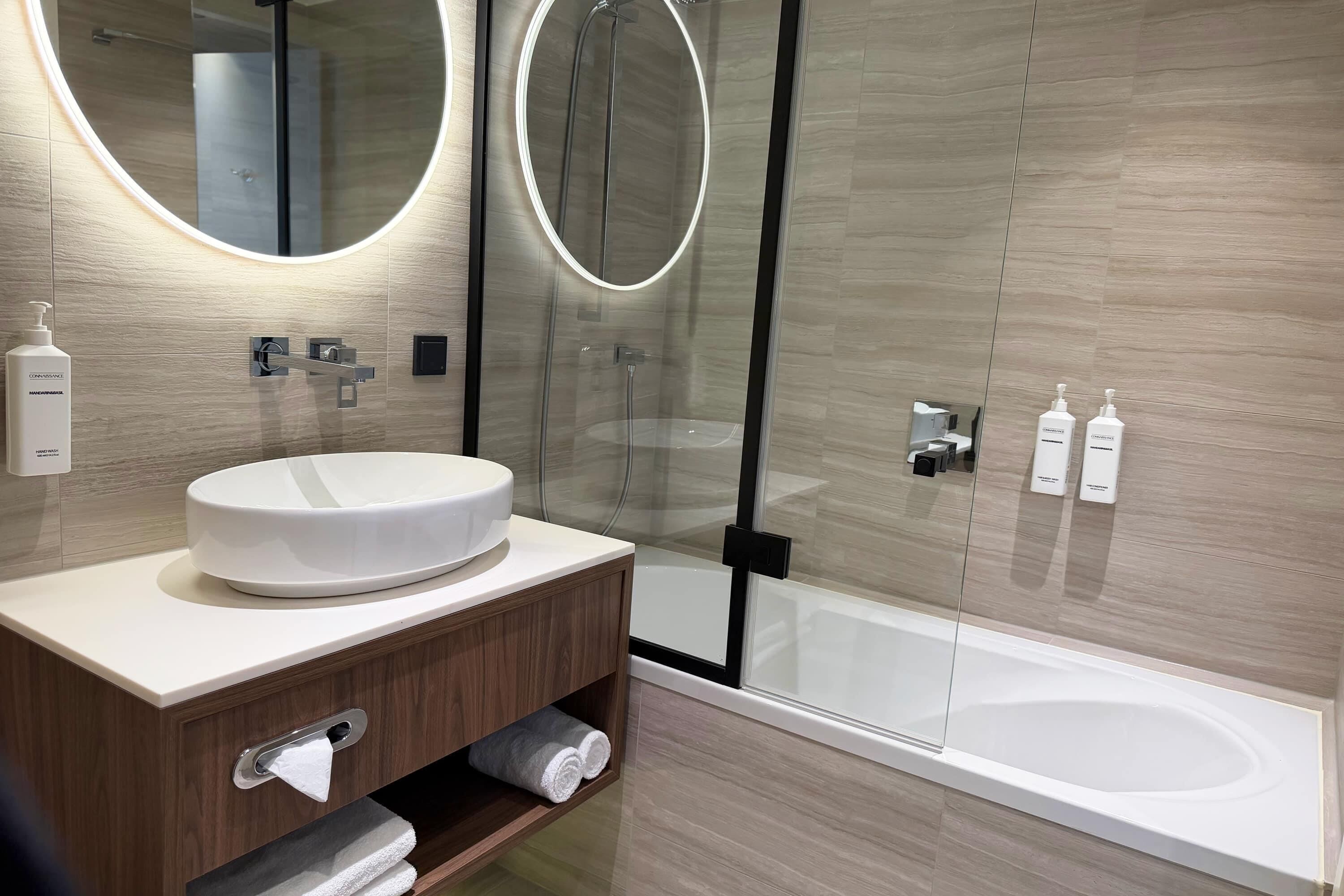 Un baño moderno con un lavamanos redondo, una ducha con cerramiento de vidrio y un espejo grande.