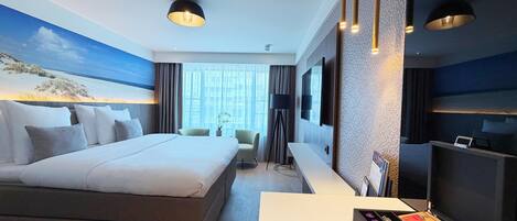 A hotel room with a bed, a desk with a coffee maker, a TV, and a painting on the wall.