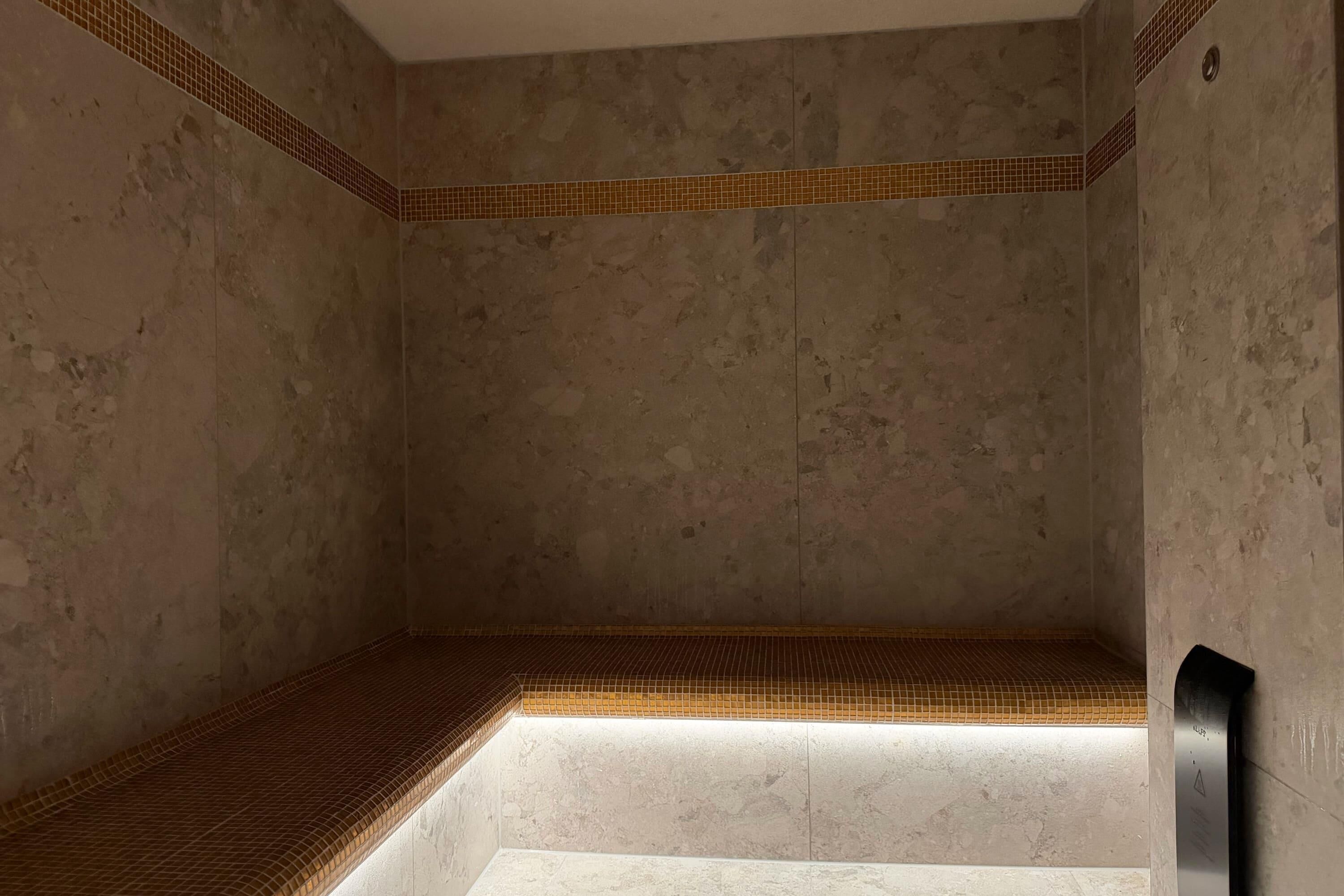 Un baño con piso de baldosas, un banco y un perchero de toallas en la pared.