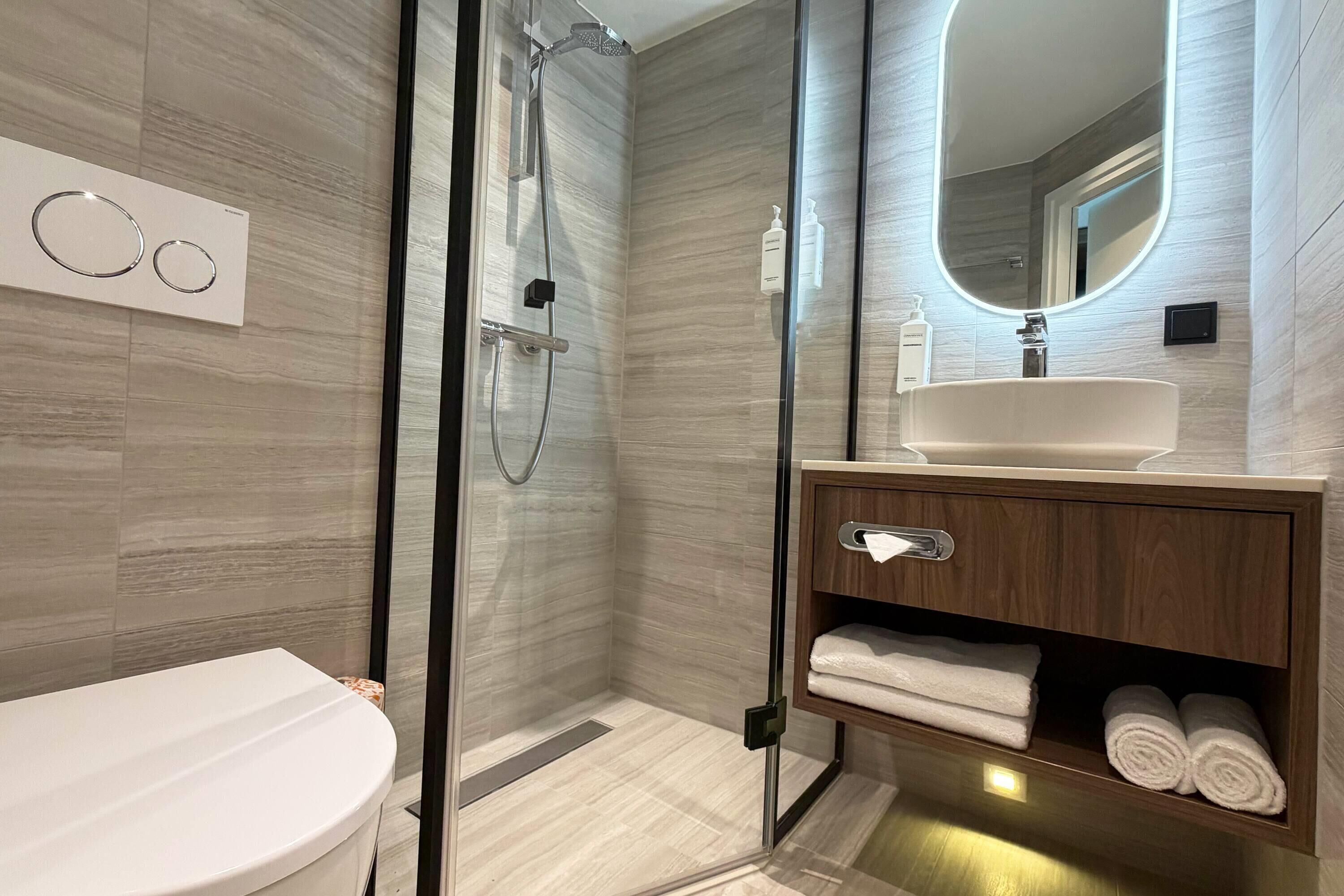 A modern bathroom with a glass-enclosed shower, a white sink, and a wooden vanity.