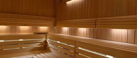 A sauna with wooden benches and slatted backrests, a visible control panel, and a wooden ceiling.